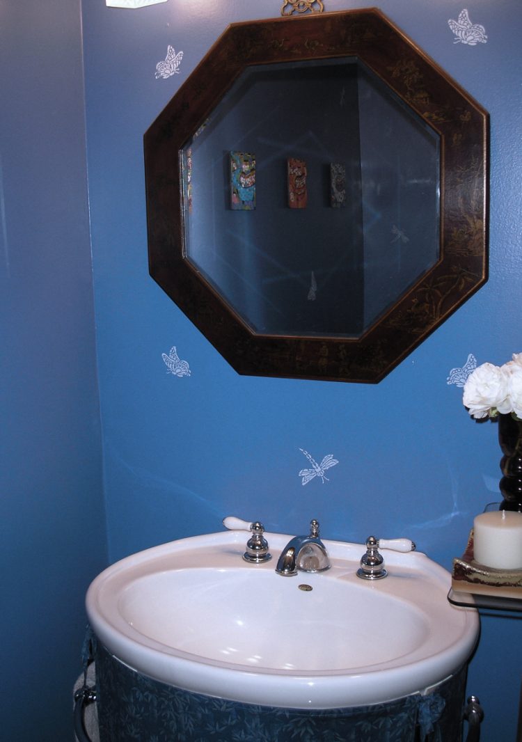 A small power room in a rich, dark blue contrasts the dark red mirror frame